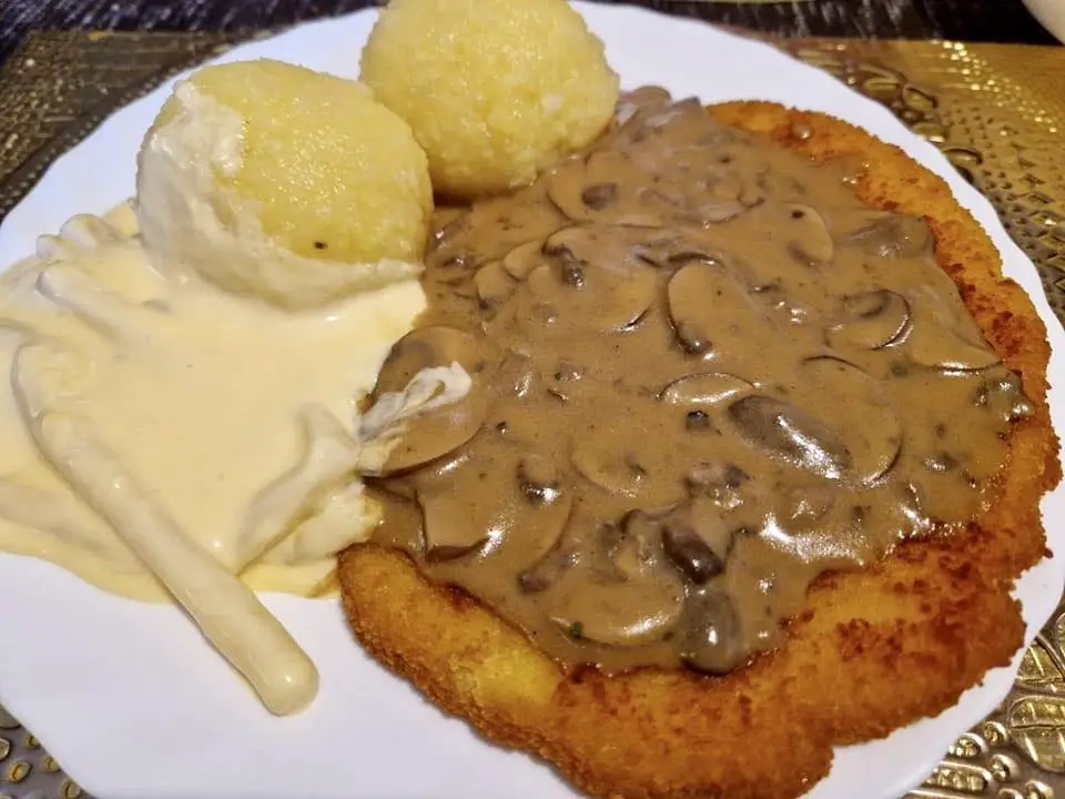 Schnitzel con funghi marroni freschi in salsa di panna, teste di asparagi in salsa olandese e gnocchi di patate